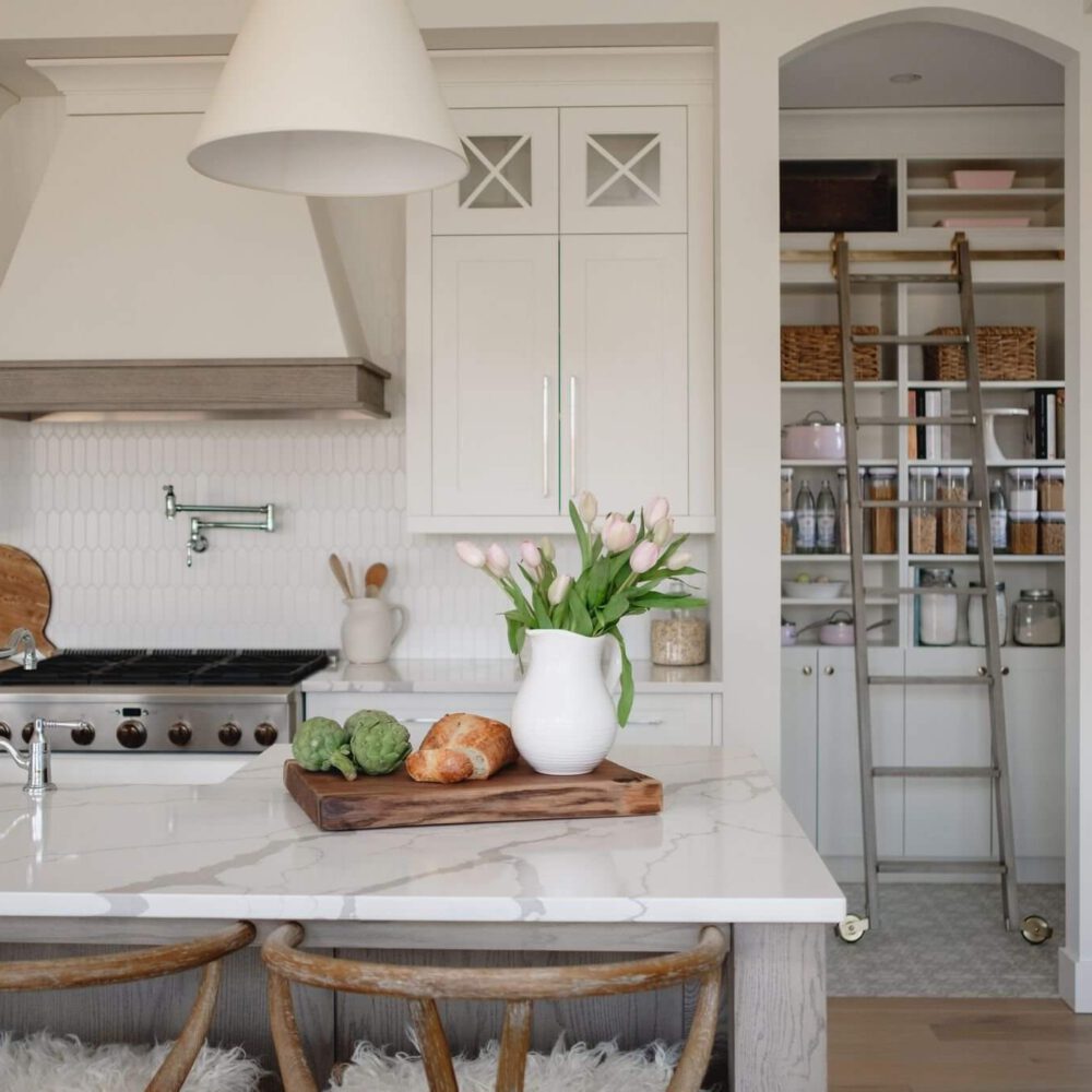 Byron Beauty kitchen by Casey's Kitchens with neutral white cabinetry, marble island, oak detailing, pendant lighting, and a walk-in pantry with a ladder