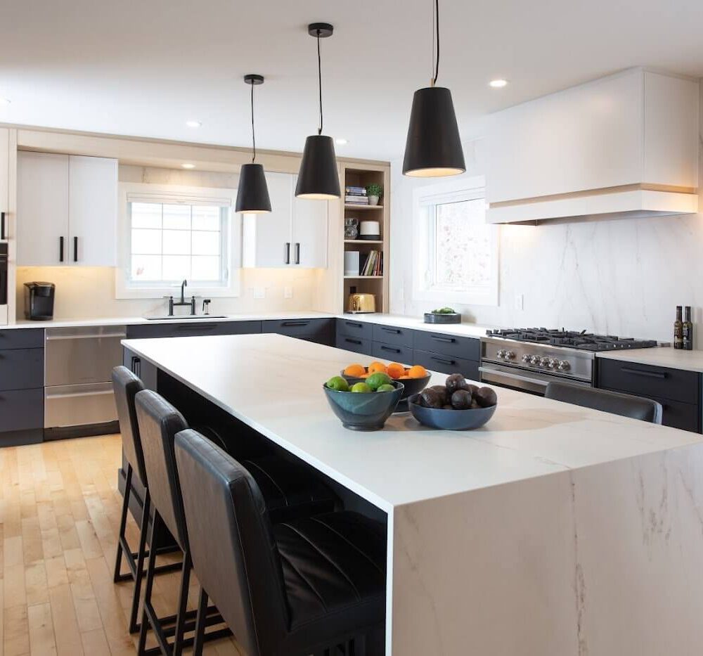 Modern kitchen with dark lower cabinets, white upper cabinets, a large marble-look island and black pendant lights.