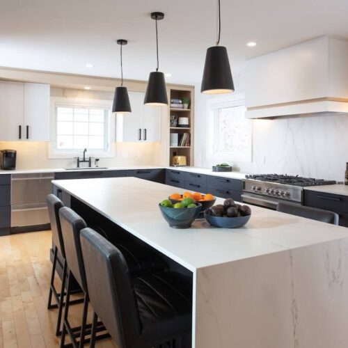 Modern kitchen with dark lower cabinets, white upper cabinets, a large marble-look island and black pendant lights.
