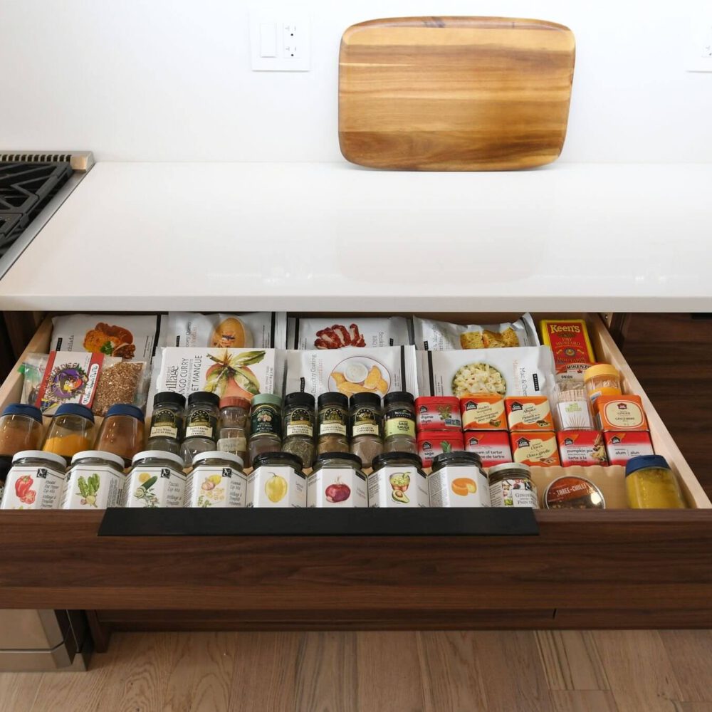 Casey's Kitchens showcases a modern contemporary kitchen with white quartz countertops and warm wood drawers, featuring an organized drawer pantry and a wooden cutting board.