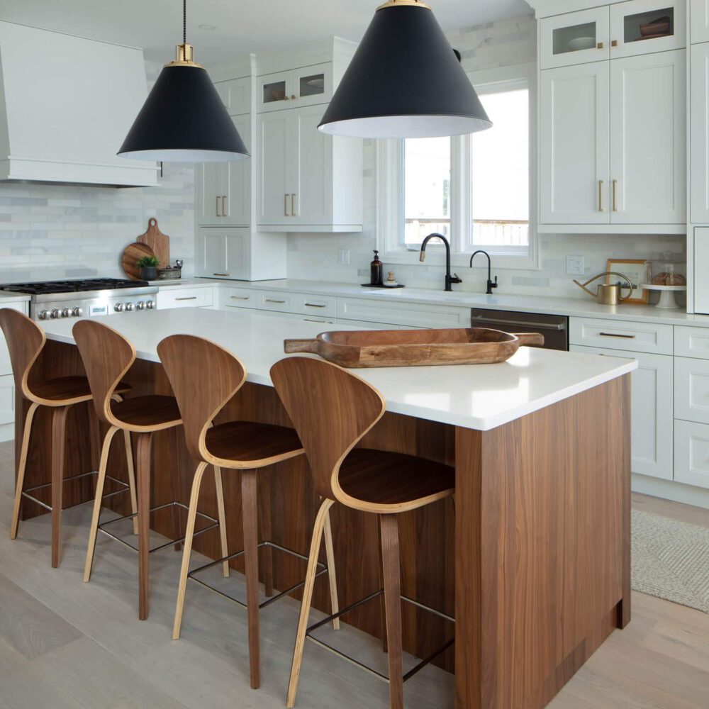 Bright custom kitchen with white cabinetry, a walnut island, black pendant lights and wood bar stools.