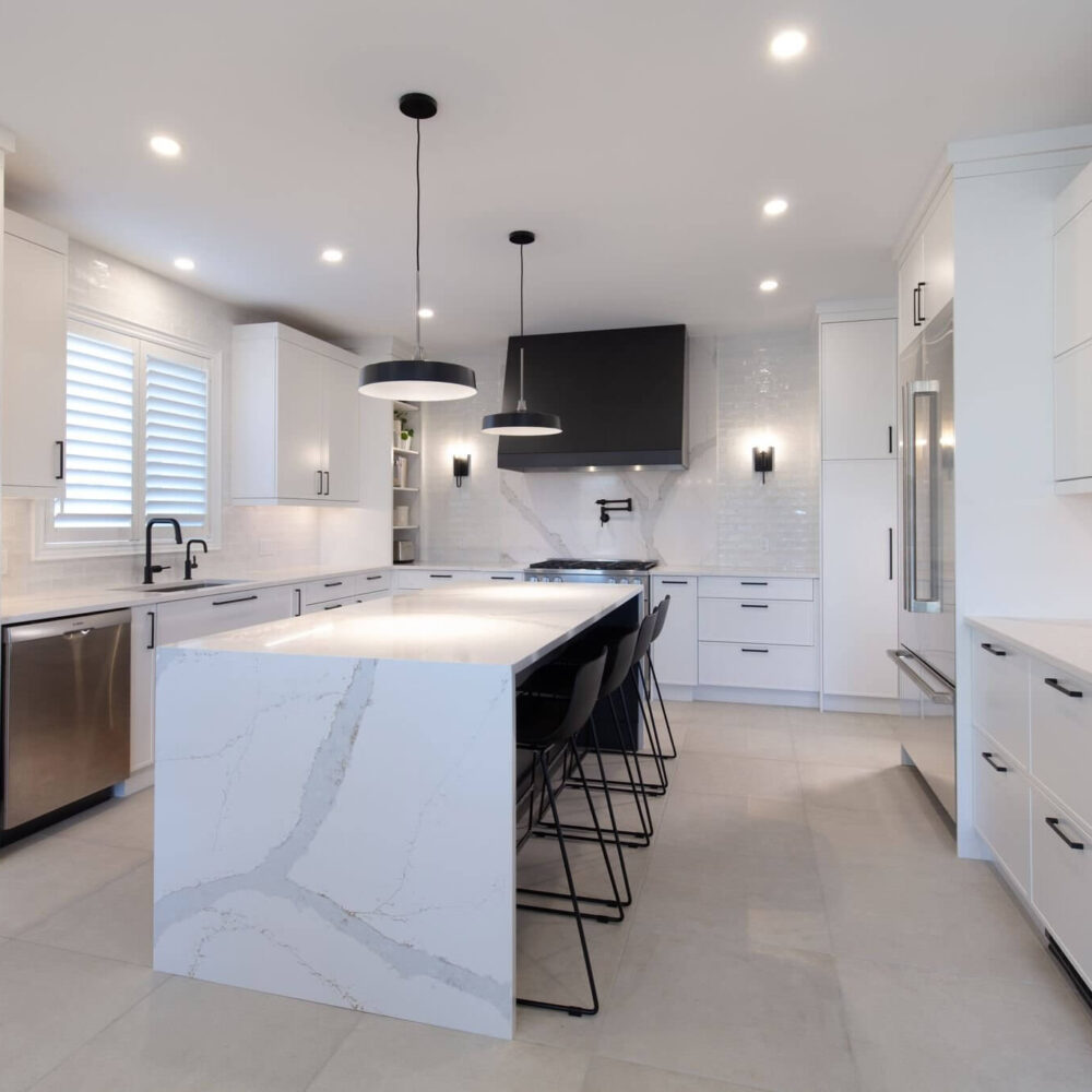 Bright white kitchen with a marble-look island, black pendant lights, black hardware, and a dark range hood.