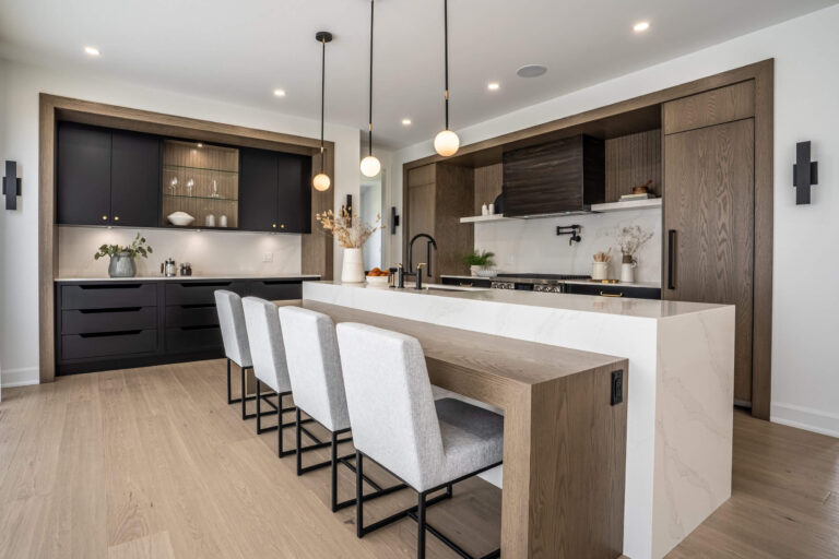 Modern kitchen with ebony cabinetry, warm oak framing, a quartz island, and three pendant lights over upholstered stools.