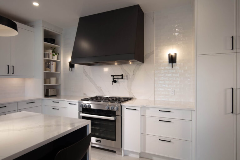 Modern white kitchen with a bold black range hood, marble-look backsplash, stainless stove and black hardware.