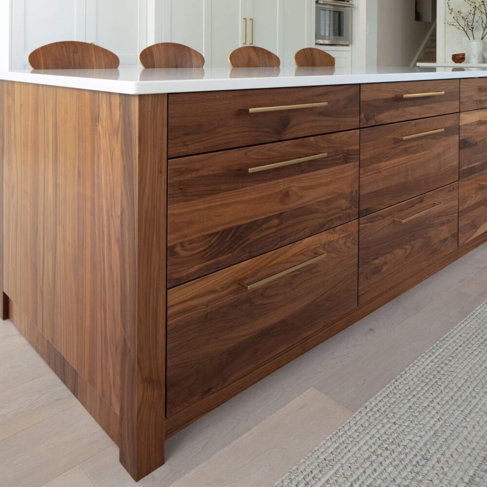 Walnut kitchen island with a white countertop and brass pulls sits in a bright modern interior with matching curved stools.