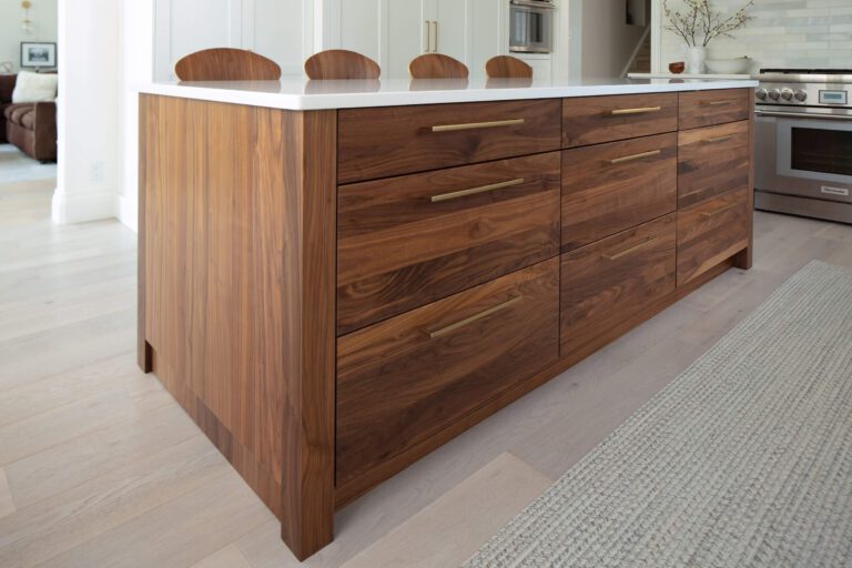 Walnut kitchen island with a white countertop and brass pulls sits in a bright modern interior with matching curved stools.