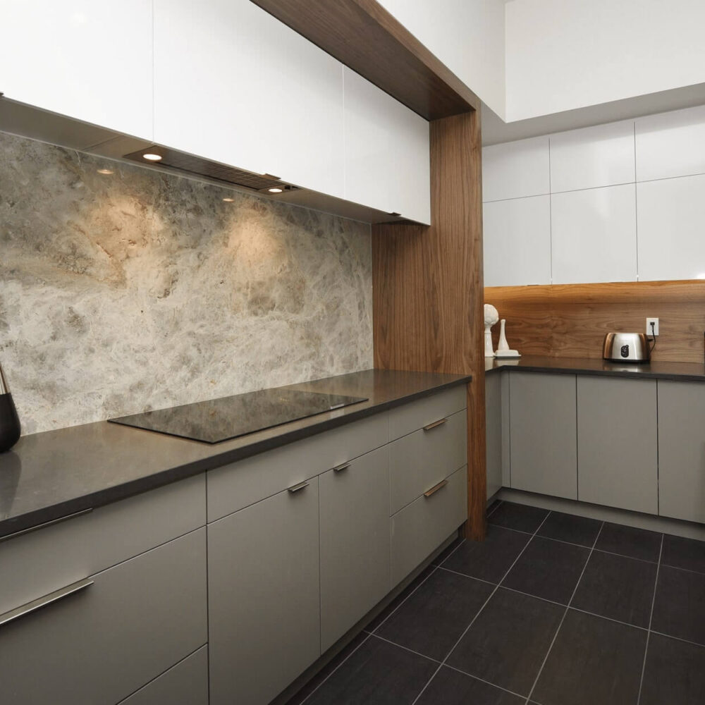 Modern kitchen design featuring sleek gray cabinetry, a stone backsplash, and stainless steel appliances.