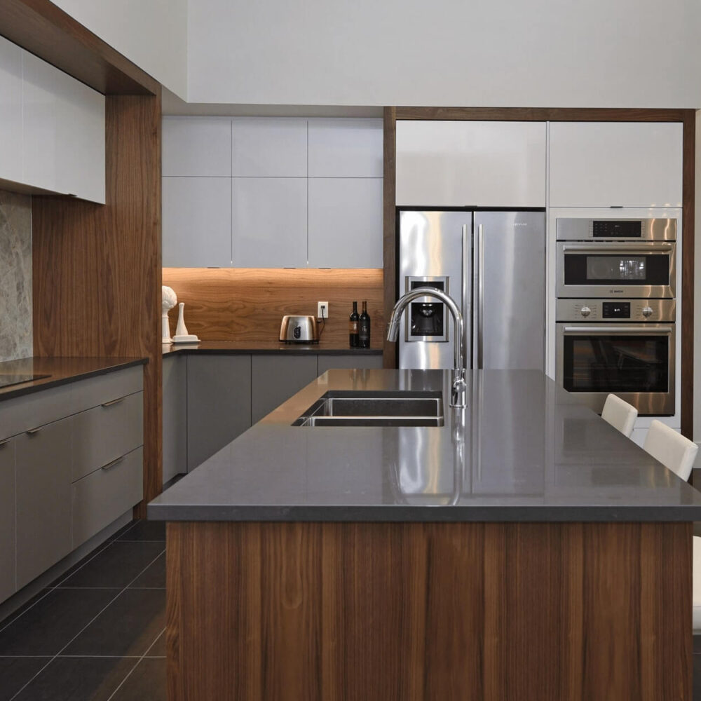 Callingham kitchen by Casey's Kitchens with high-gloss white upper cabinets, walnut wood posts, a large gray island, stainless steel appliances, and a marble backsplash in a London, Ontario home