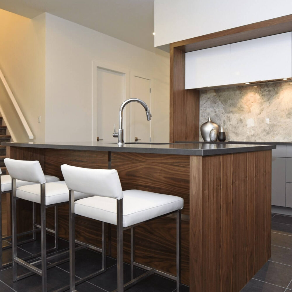 Callingham kitchen by Casey's Kitchens with high-gloss white cabinets, warm walnut island, gray countertop, marble backsplash, and a modern chrome faucet