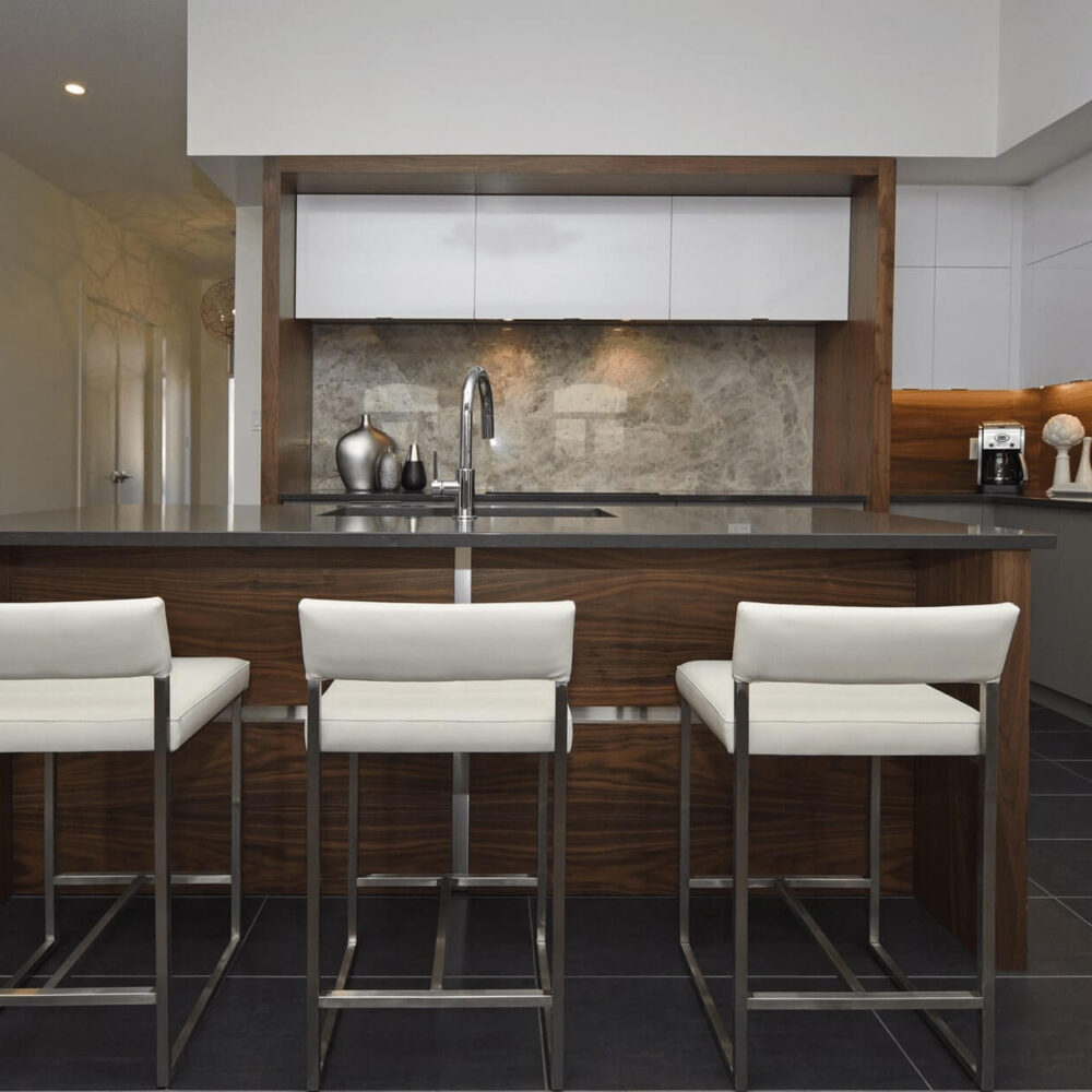 Modern kitchen with a central island featuring three white bar stools and sleek cabinetry.