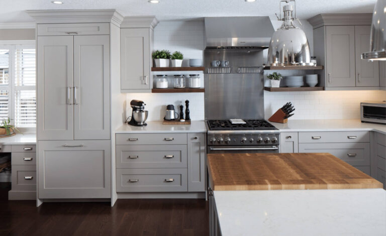 Modern kitchen with gray cabinetry, stainless steel appliances, and a wooden countertop. Features a gas range, mixer, and open shelving.