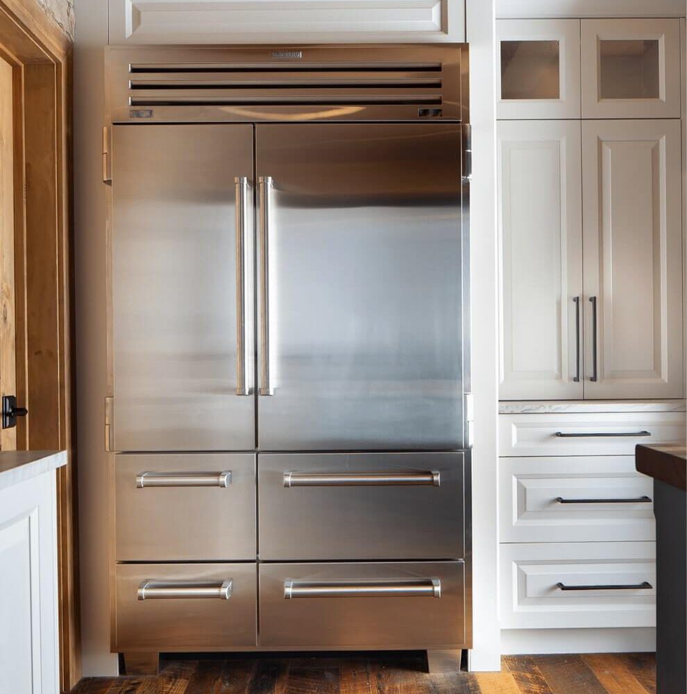 Stainless steel refrigerator with double doors and a sleek design, positioned next to white cabinetry in a modern kitchen.