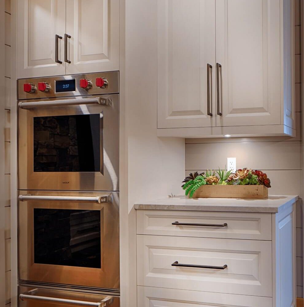 Modern kitchen cabinetry with double ovens, sleek white finish, and a countertop displaying a small arrangement of succulents.