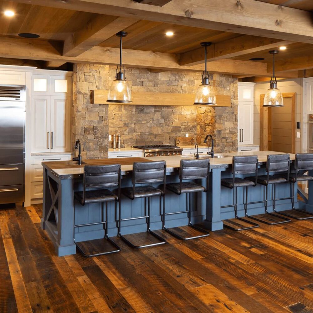 Modern kitchen with a large island, wooden beams, stone accents, and stainless steel appliances, featuring bar stools along the island.
