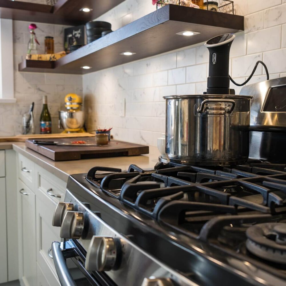 Old South Kitchen project by Casey's Kitchens with a stainless steel gas range, large pot on the stove, white subway tile backsplash, and dark walnut floating shelves.