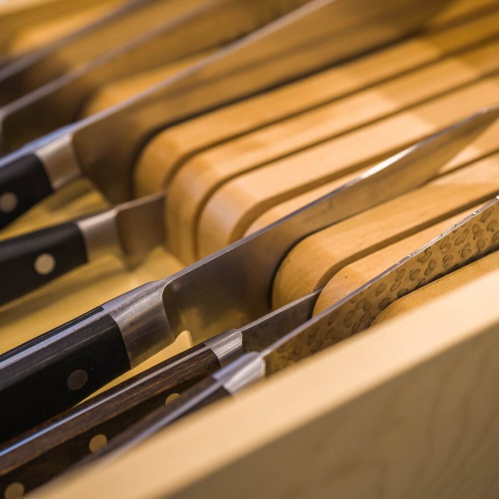 Old South Kitchen close-up of knife block and chef knives with wooden handles and metallic blades, showcasing warm wood tones and precision hardware in a Casey's Kitchens project with Chad Stewart.