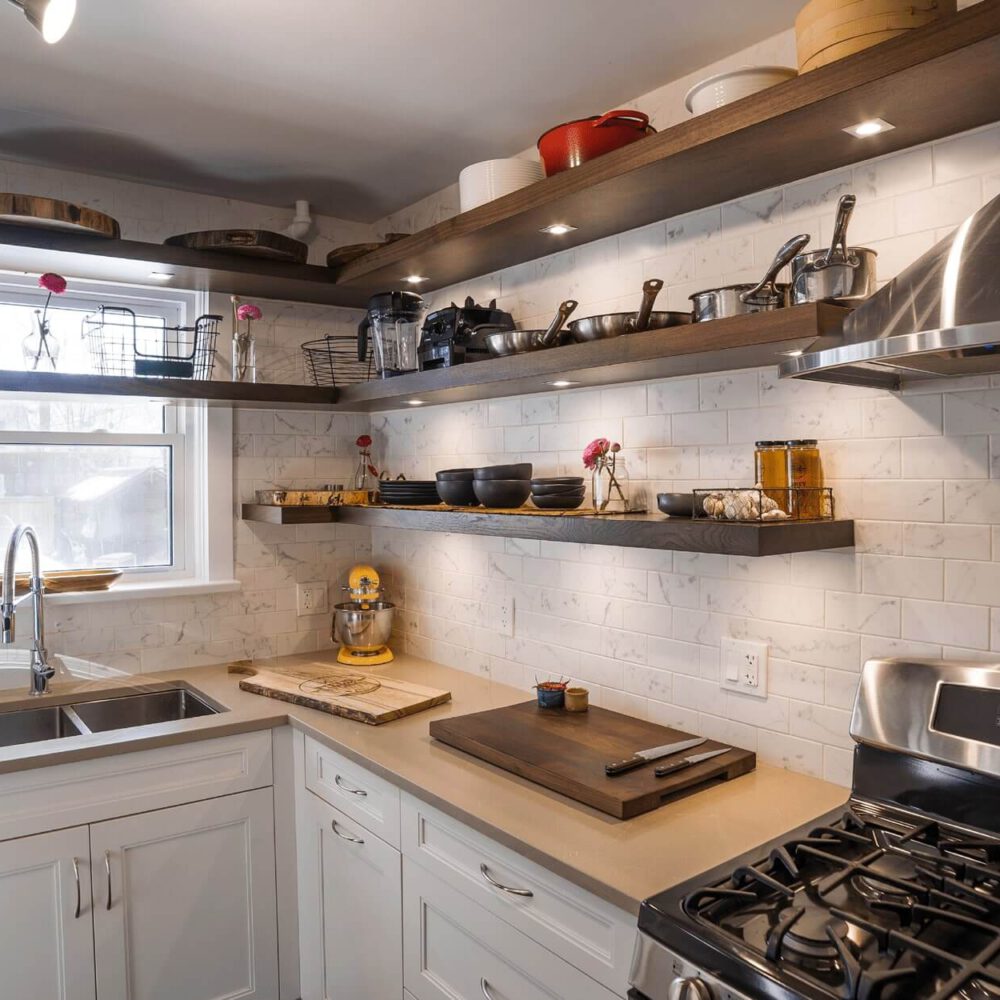 Old South Kitchen by Casey's Kitchens featuring walnut floating shelves, white cabinetry, stainless steel appliances, and a bright window with pink flowers—Chad Stewart’s project in London.
