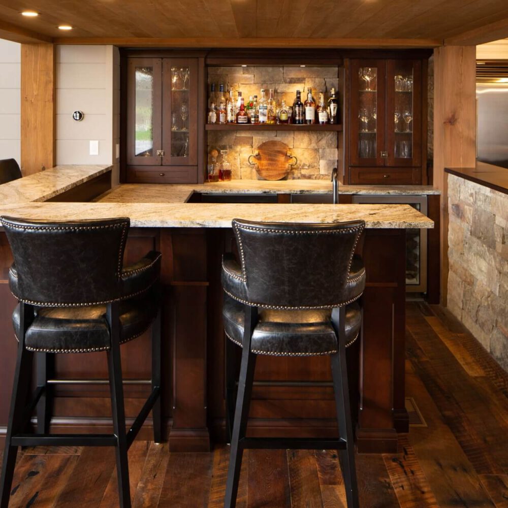 Rustic wood bar cabinetry with glass doors, a stone backsplash wall, and a counter setup for bottles in the Fruit Ridge project.