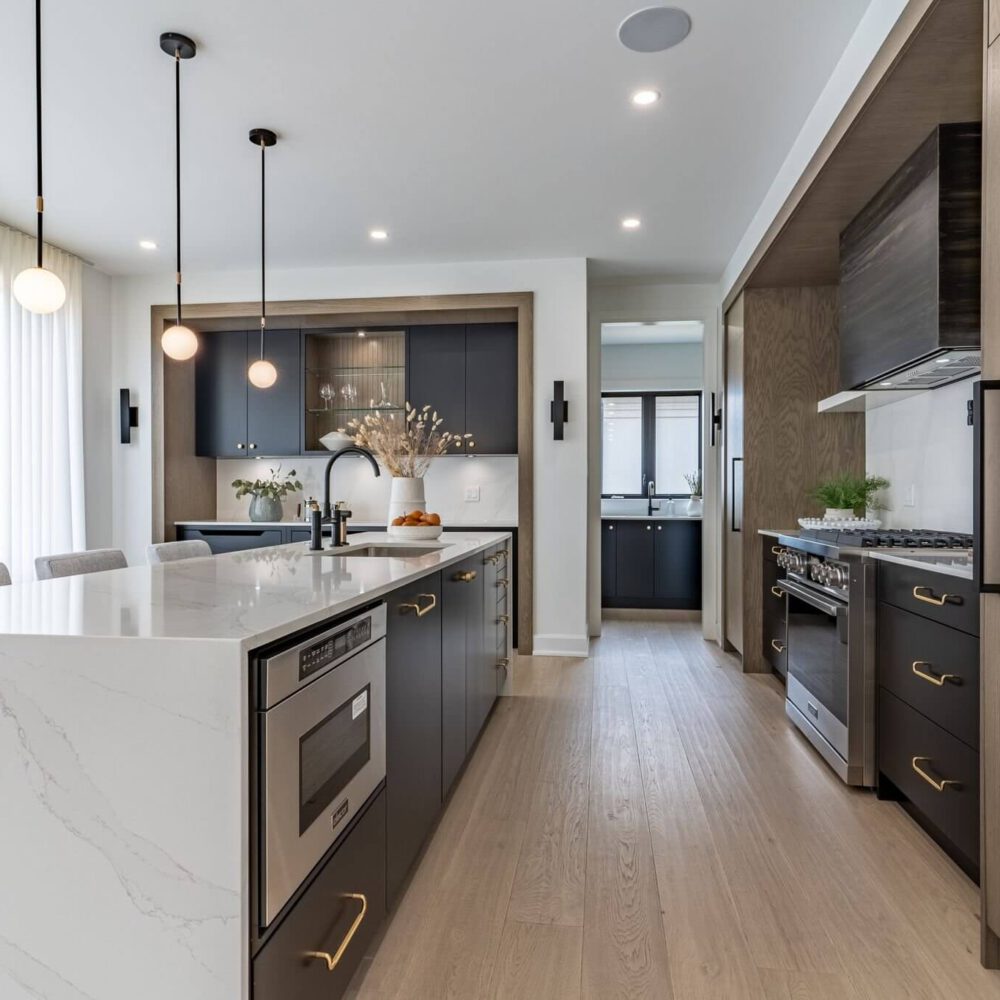 A modern London Dream Home kitchen with a white quartz island, dark cabinetry, oak paneling, and black pendant lights.