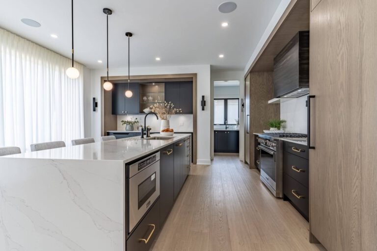 A modern London Dream Home kitchen with a white quartz island, dark cabinetry, oak paneling, and black pendant lights.