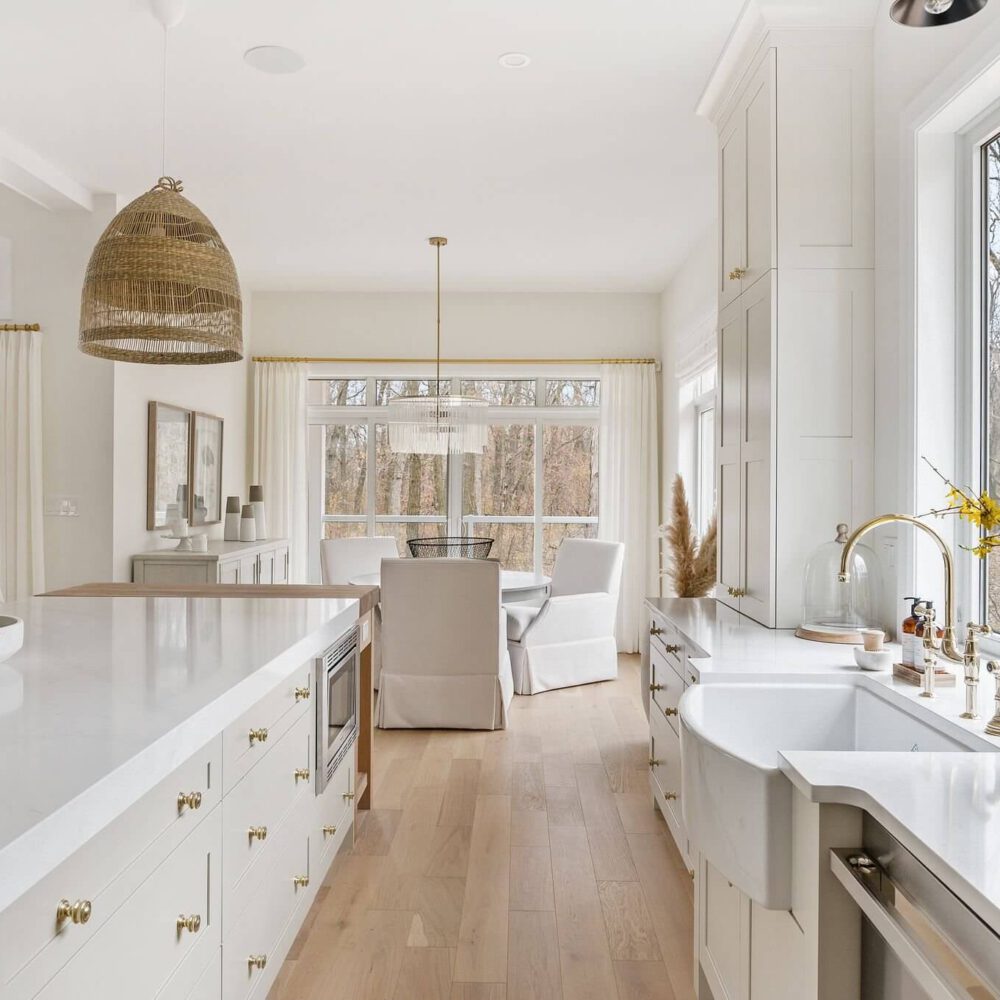 Bright modern kitchen featuring white cabinetry, a large island, and a farmhouse sink with natural light streaming through windows.