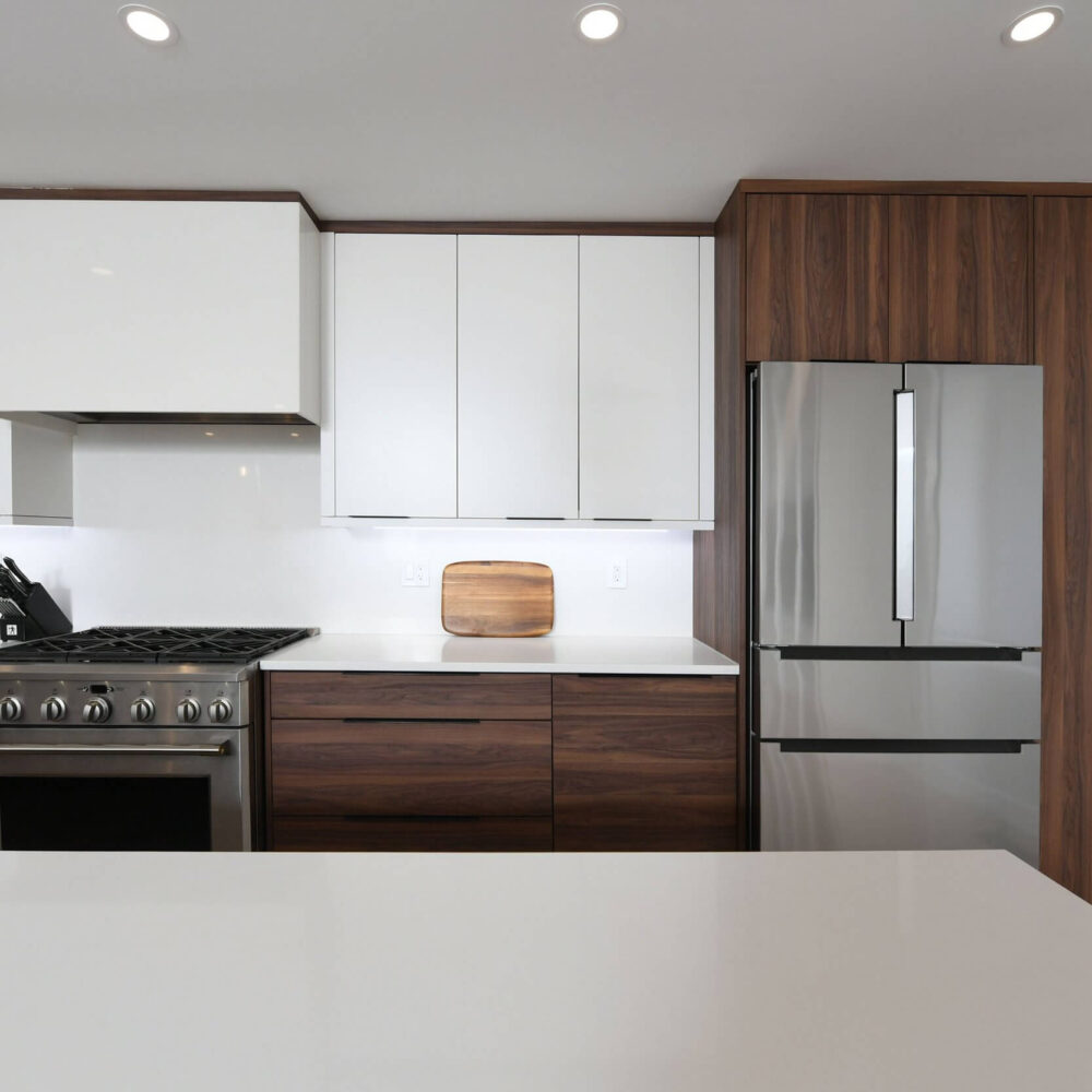 Modern kitchen with white upper cabinets and dark wood lower cabinets, stainless steel refrigerator and range, white countertops, and a wooden cutting board on the counter