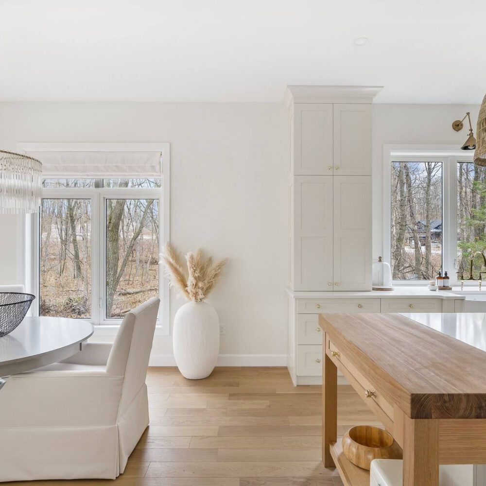 Bright modern kitchen featuring a round dining table, white chairs, and a wooden island with a natural finish.
