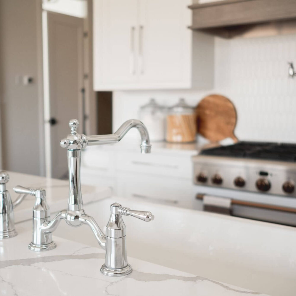 Chrome kitchen faucet and sink in a white, modern kitchen with a stainless steel stove and light cabinetry, reflecting a Byron Beauty style by Casey's Kitchens