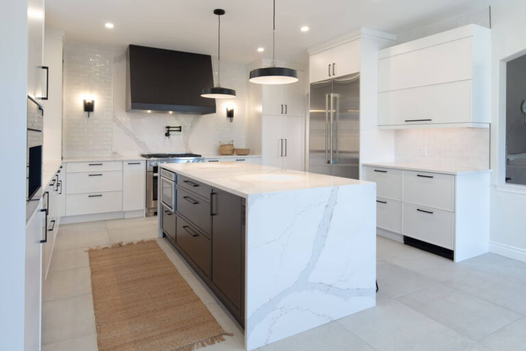 Modern white kitchen with a large marble island, black range hood, stainless steel fridge, and brass woven rug.