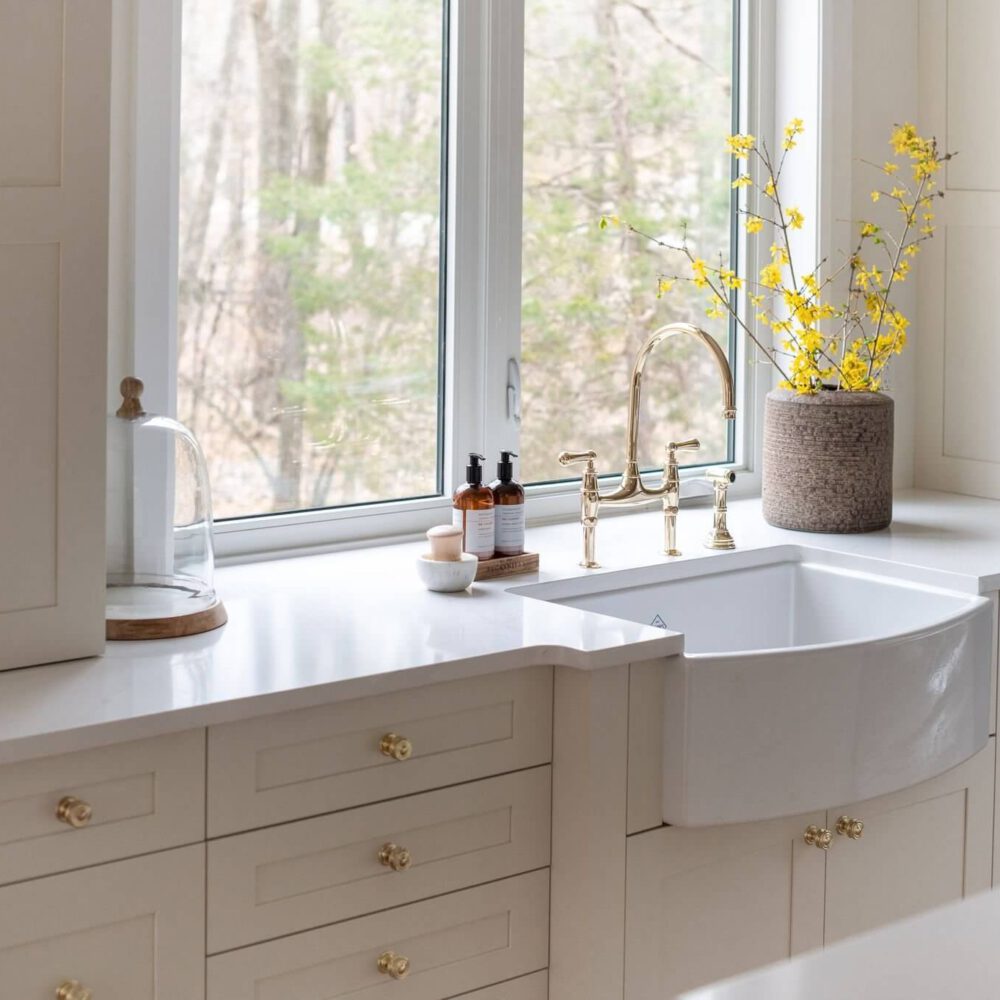 White farmhouse sink with a gold faucet and decorative vase on a kitchen countertop.