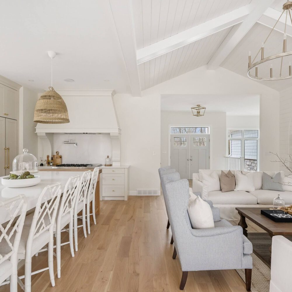 Bright modern kitchen with white cabinetry and a large island, featuring a dining area with chairs.
