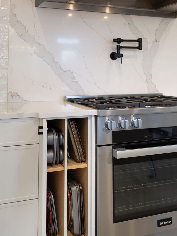 A stainless steel Miele range sits below a marble-look backsplash with a pot filler and slim cabinet storage.