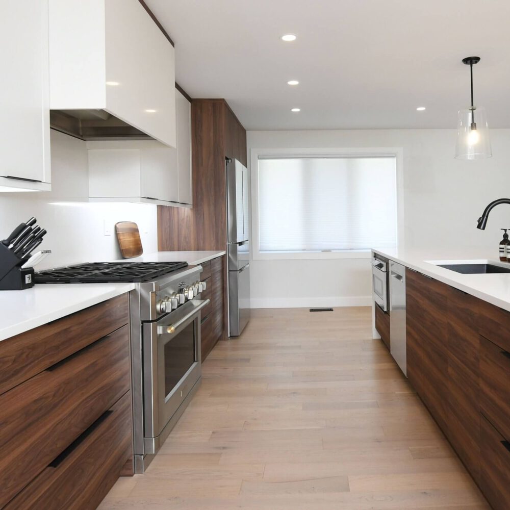 Modern contemporary kitchen by Casey's Kitchens with white upper cabinets, rich wooden lower cabinetry, stainless steel appliances, and a large white island featuring a black faucet and sink.