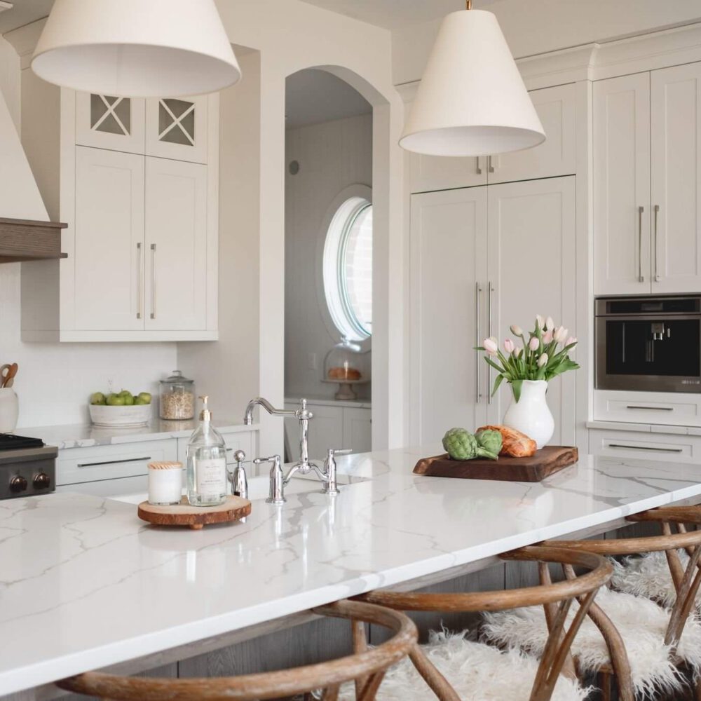 White modern farmhouse kitchen with a marble island, white cabinetry, and wooden bar stools, featured in Byron Beauty by Casey's Kitchens in London.