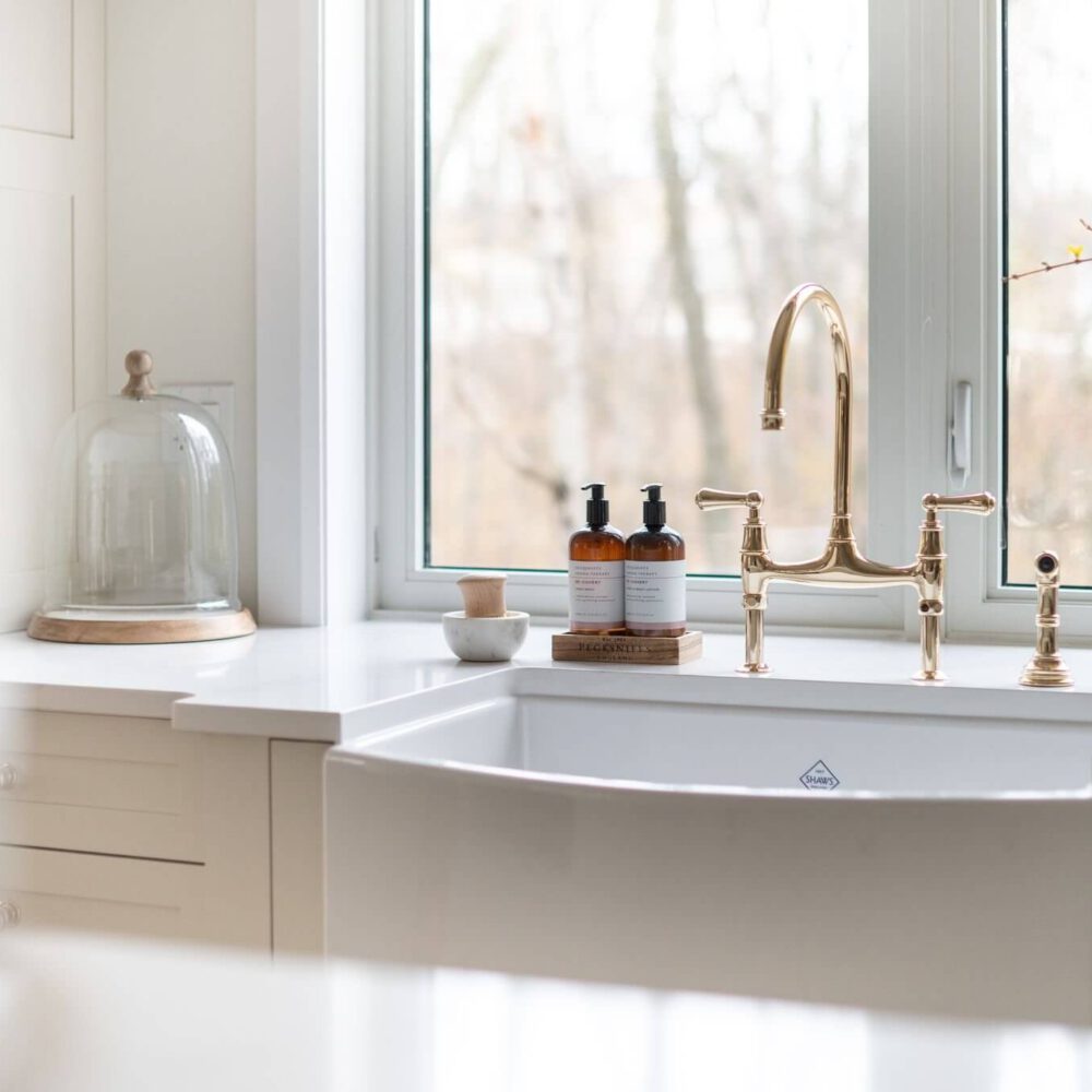 White farmhouse sink with a gold faucet and decorative items on the countertop.