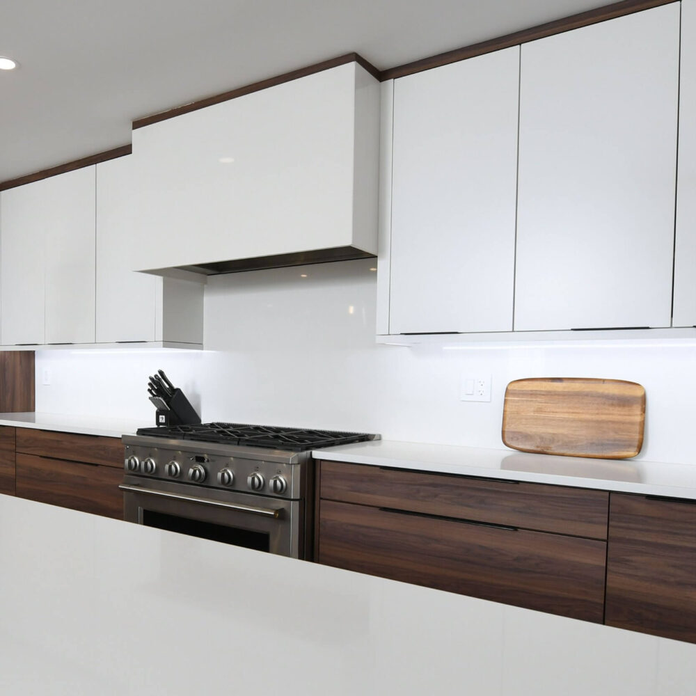 Modern contemporary kitchen by Casey’s Kitchens featuring white upper cabinets, dark wood lower cabinets, stainless steel range, bright lighting, and a wooden cutting board on the counter