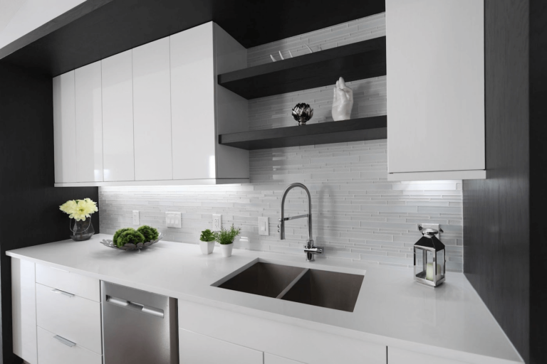 Modern kitchen design featuring a white countertop, stainless steel sink, and minimalist cabinetry with decorative plants and a lantern.