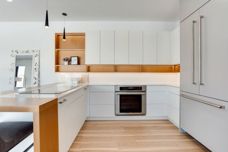 Modern kitchen with white cabinetry, wooden accents, and stainless steel appliances, featuring a sleek design and open layout.